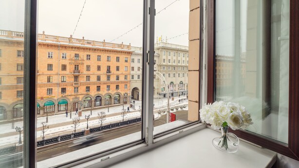Ett fönster med utsikt över en stad, en vas med blommor och en snötäckt gata.