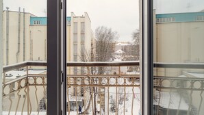 En utsikt från en balkong med metallräcken, med utsikt över ett snötäckt stadsområde med byggnader och kala träd.