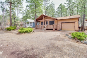 A cabin with a porch, a garage, and a gravel driveway surrounded by trees.