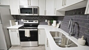 A modern kitchen with stainless steel appliances, white cabinetry, and a grey tiled backsplash. - Beautiful Suite King Bed|Long Stays|Disney|Airport (Edmonton)