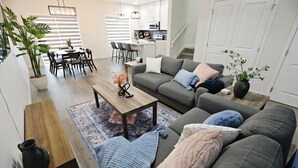 Un salon moderne avec un canapé gris, une table basse en bois et un coin repas comprenant une table et des chaises.