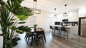 Une cuisine moderne avec une table à manger en bois, des tabourets de bar et des luminaires suspendus.