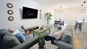 Un salon moderne avec un canapé gris, une table basse agrémentée d’une plante et un téléviseur fixé au mur qui diffuse l’émission « Glitter Lifestyle ».
