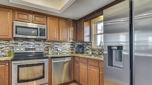 A modern kitchen with stainless steel appliances, wooden cabinets, and a tiled backsplash. - Pool, Beach Access: Waterfront Treasure Island Gem (Treasure Island)