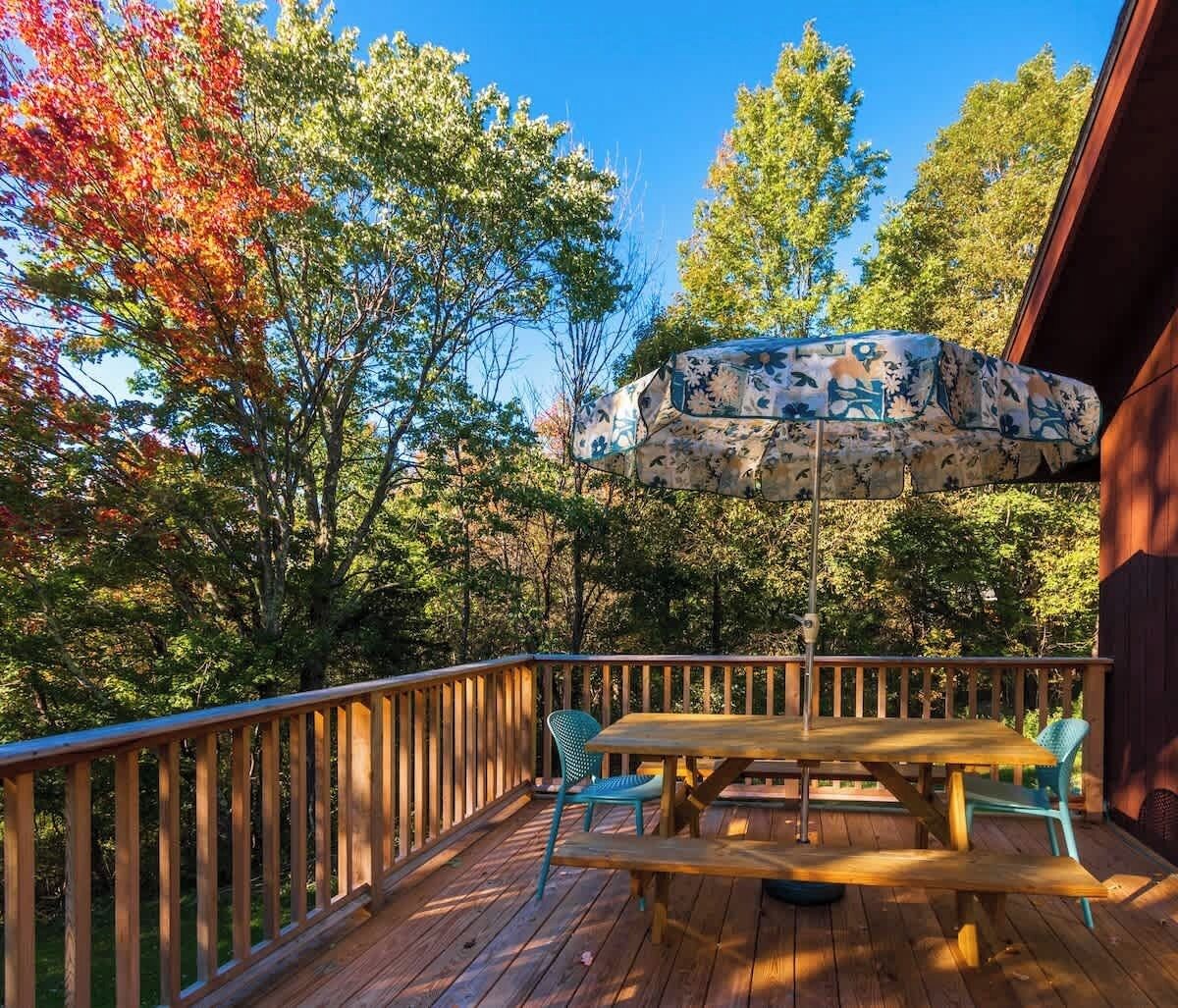 Une terrasse en bois avec une table et des chaises, entourée d’arbres aux feuilles d’automne.