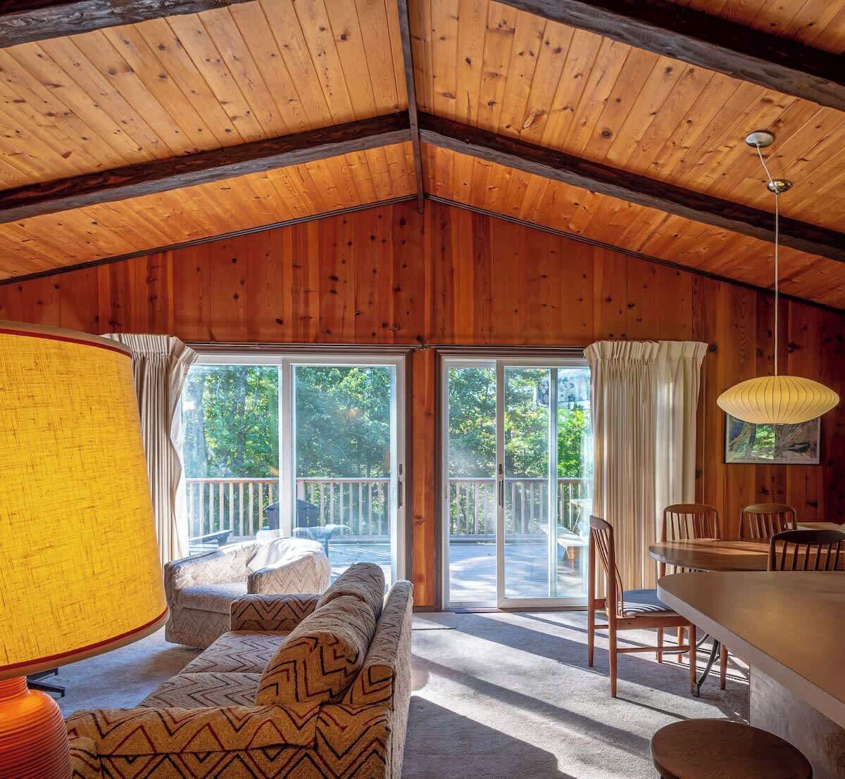 Ein gemütliches Blockhausschlafzimmer mit Holzbalkendecke, einer Couch, einem Esstisch mit Stühlen und einem großen Fenster mit Ausblick.