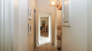 A narrow hallway with a tiled floor, white walls, and a door leading to a living area. - The Courtyard (Carlisle)