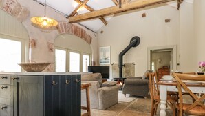 A rustic interior with exposed wooden beams, a stone fireplace, and a dining area with wooden chairs and a table. - The Courtyard (Carlisle)
