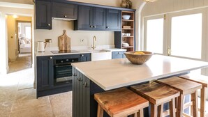 A modern kitchen with dark cabinetry, a central island, and wooden stools. - The Courtyard (Carlisle)