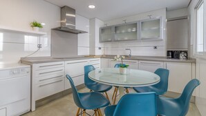 A modern kitchen with white cabinets, a stainless steel range hood, and a glass dining table with blue chairs.