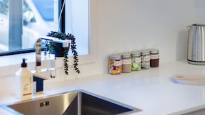 Eine moderne Küche mit einem Edelstahl-Spülbecken, einer Kaffeemaschine und mehreren Gläsern mit Gewürzen auf der Arbeitsfläche.