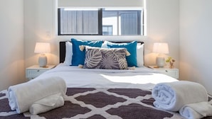 Ein ordentlich bezogenes Bett mit blauen und gemusterten Kissen, zwei Nachttischlampen und einem braun-weißen Teppich.