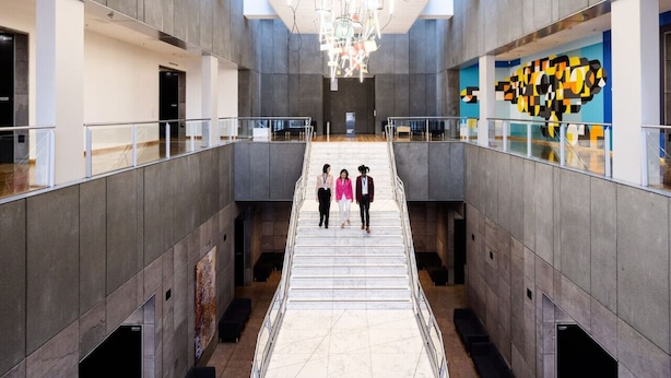 A modern interior with a central staircase, glass railings, and a large abstract mural on the right wall.