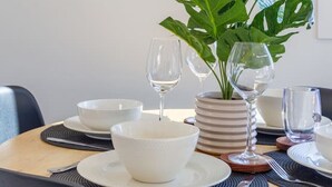 Ein Esstisch, gedeckt mit weißen Schüsseln, Tellern und Weingläsern, mit einem Blumentopf mit großen, grünen Blättern.