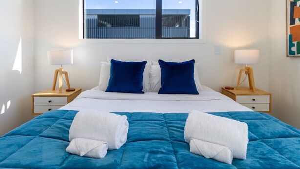 Ein Hotelzimmer mit einem großen Bett, zwei Nachttischen, zwei Lampen und einem Fenster mit Blick auf ein Gebäude.