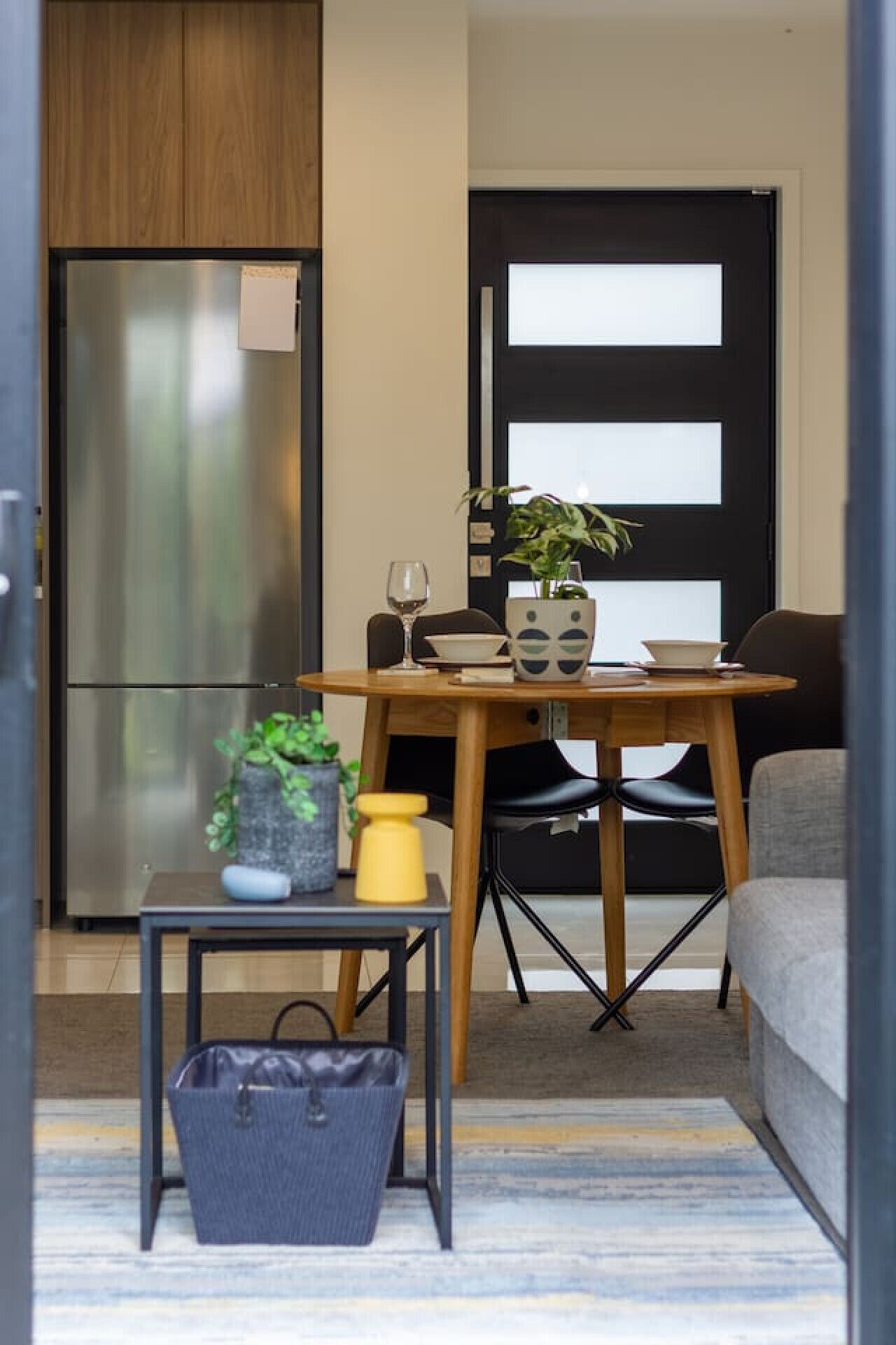 A compact living space with a kitchenette, a dining area with a table and chairs, a sofa, and a small side table with a plant and a yellow object.