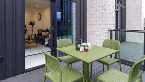 Et grønt metalbord og stole på en balkon med udsigt over en moderne bygning og en stue.
