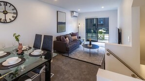 En moderne stue med et glasbord dækket til fire personer, en sofa, et sofabord og et stort vægur.