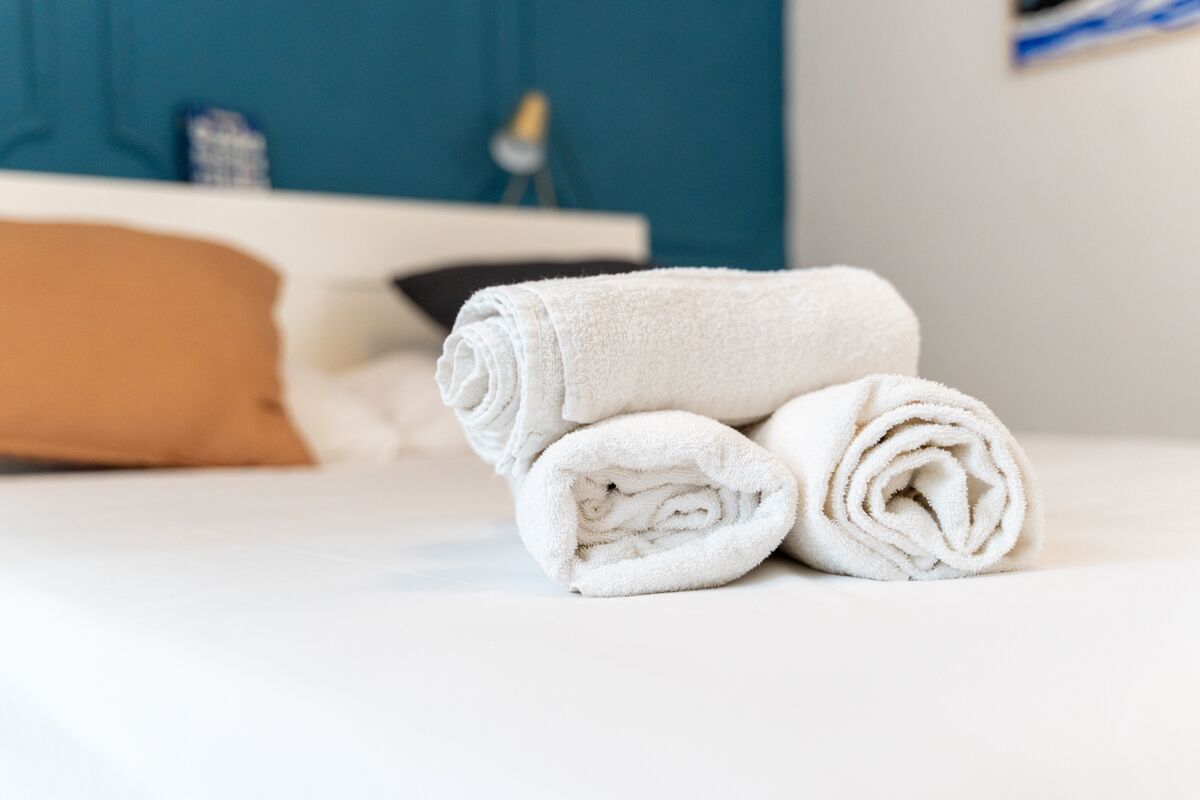 A neatly made bed with white and brown pillows, a folded white towel, and a teal-colored wall in the background.