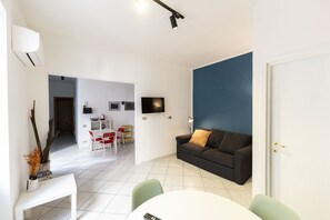 Una sala de estar moderna con un sofá blanco, una mesa de comedor y un televisor montado en la pared.