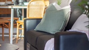 Ein modernes Wohnzimmer mit einer schwarzen Couch, einem kleinen runden Tisch, einer Essecke mit Tisch und Stühlen sowie einer Topfpflanze.