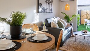 Ein modernes Wohnzimmer mit einem runden Esstisch für zwei Personen, einem Ledersofa und Blick auf den Garten.