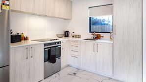 Eine moderne Küche mit hellen Holzschränken, einem Edelstahlkühlschrank, einem Einbauofen und einem großen Fenster über der Spüle.