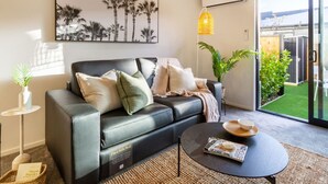 Ein modernes Wohnzimmer mit einer schwarzen Ledersofa, einem Couchtisch und einem großen Fenster mit Blick auf einen Garten.