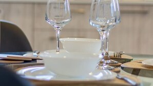 A dining table with two wine glasses and a bowl, set in a modern kitchen with a window in the background.