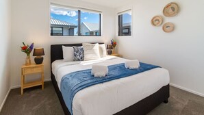 A neatly arranged bedroom with a large bed, two bedside tables, a window, and a view of buildings outside.