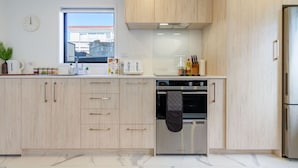 A modern kitchen with light wood cabinets, a built-in oven, and a stainless steel refrigerator.