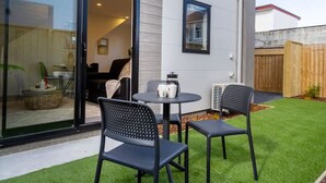 A modern house with a patio featuring a table and chairs, a sliding glass door, and a well-maintained lawn.