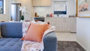 Eine moderne Küche mit hellen Holzschränken, einem Edelstahlkühlschrank sowie einer Essecke mit einem blauen Sofa und einem rosafarbenen Kissen.