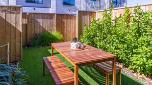 A wooden deck with a table and benches, surrounded by a wooden fence and greenery.