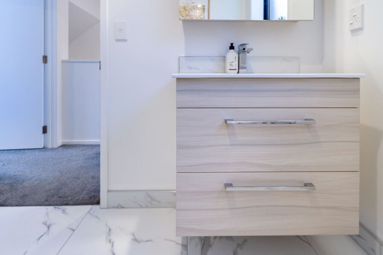 A modern bathroom with a marble floor, a white vanity with a mirror, and a small shelf with toiletries.
