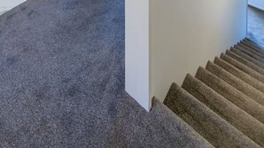 A modern interior with a carpeted staircase, a visible bedroom with a bed and nightstand, and a glass shower area.
