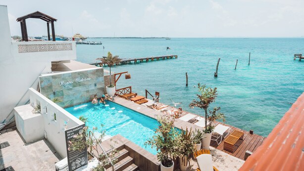 A pool area with a view of the sea, a wooden deck, and a pergola. - Bartolome Oceanfront Suites (Isla Mujeres)