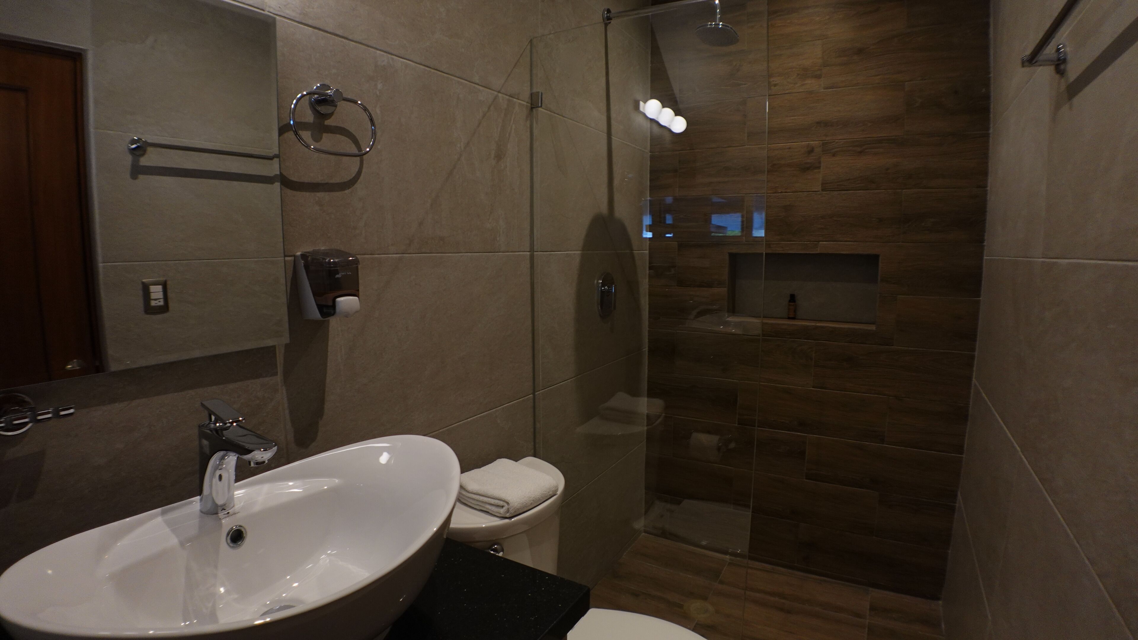 Un baño moderno con un lavamanos grande, inodoro y ducha con mampara de vidrio.