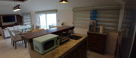 A kitchen with granite countertops, a built-in microwave, a water dispenser, and a refrigerator.