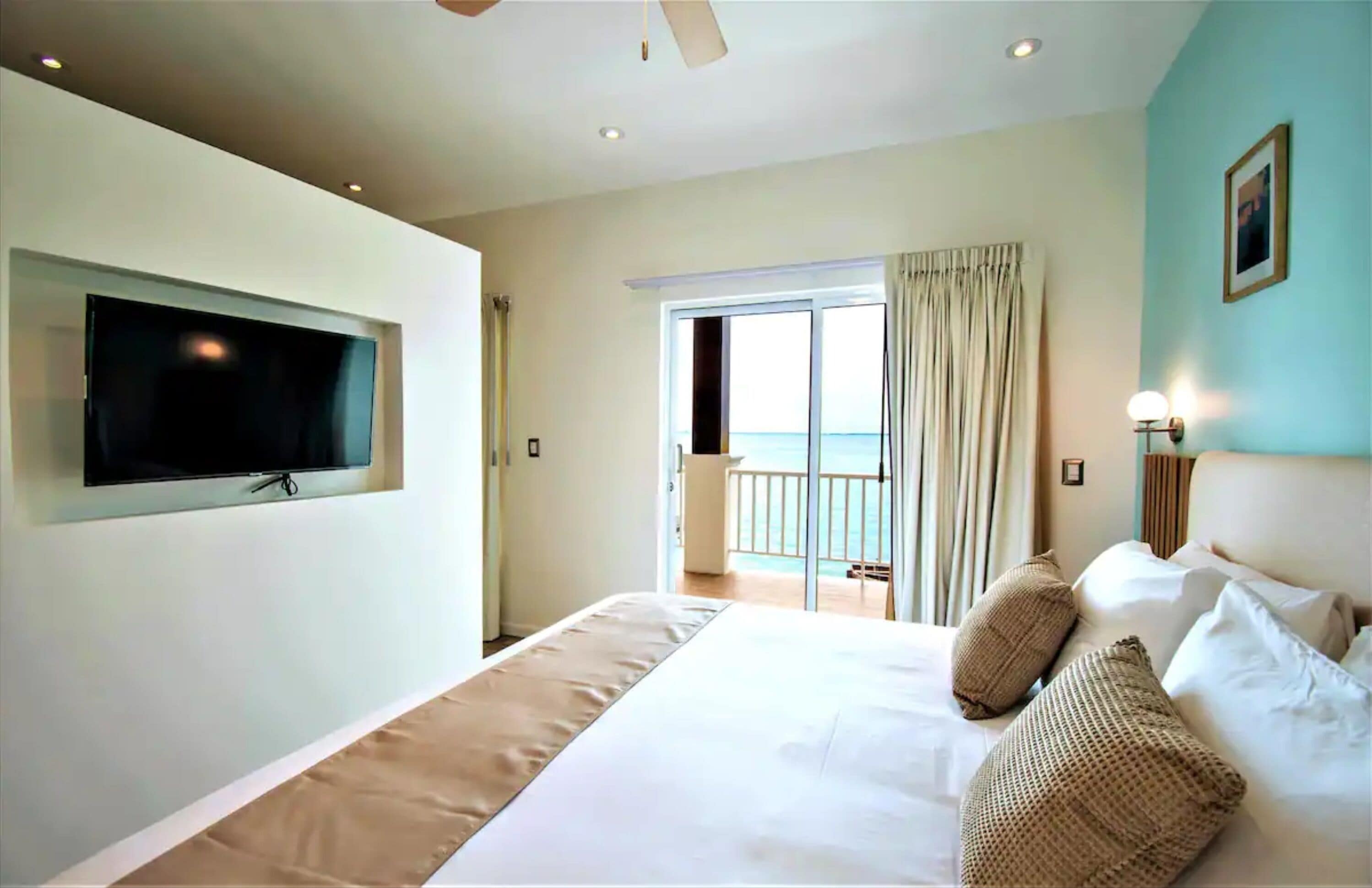Ein Hotelzimmer mit einem großen Bett, einem an der Wand montierten Fernseher, einem Balkon mit Vorhängen und Meerblick.