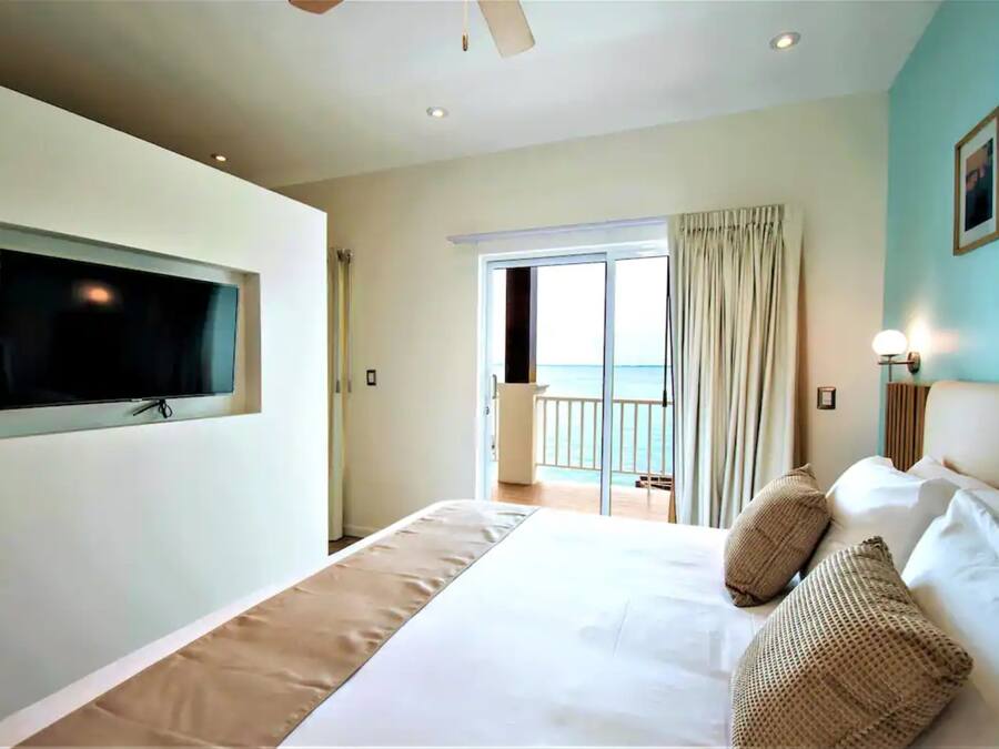 Ein Hotelzimmer mit einem großen Bett, einem an der Wand montierten Fernseher, einem Balkon mit Vorhängen und Meerblick.