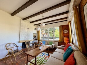 Uma sala de estar aconchegante com um sofá, cadeiras, uma mesa de madeira e uma lareira.