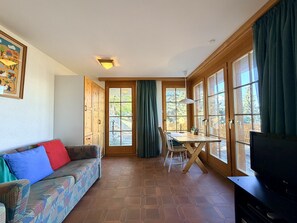 Ein gemütliches Wohnzimmer mit einer Couch, einem Esstisch und großen Fenstern.