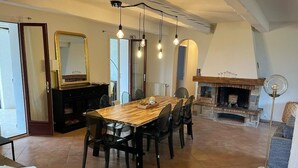 A dining area with a wooden table and chairs, a fireplace, and a mirror on the wall. - Superbe Propriété Avec vue Imprenable, Piscine, jeu de Boules au Cœur du Luberon (Saint Saturnin lès Apt)