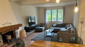 A cozy living room with a fireplace, a sofa set, a dining table, and a television. - Superbe Propriété Avec vue Imprenable, Piscine, jeu de Boules au Cœur du Luberon (Saint Saturnin lès Apt)