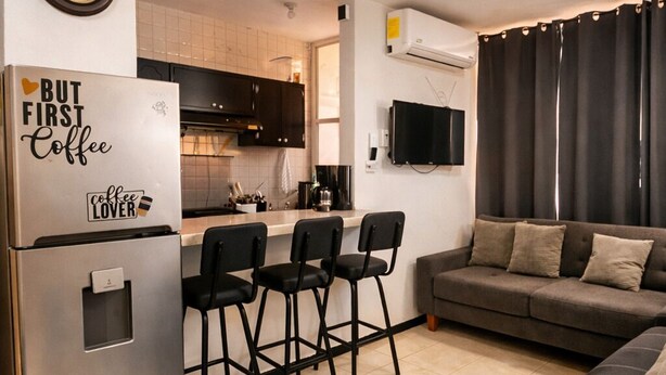 A compact living space with a kitchenette, a dining area with chairs, a sofa, and a flat-screen TV mounted on the wall.
