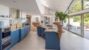 Une cuisine moderne avec des armoires bleues, un grand îlot central et une vue sur l’extérieur.