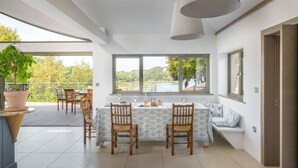 Un espace de repas moderne avec une table dressée pour deux personnes, de grandes fenêtres offrant une vue sur un lac et un balcon agrémenté d’une plante en pot.