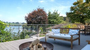 Une terrasse avec un foyer, un canapé agrémenté de coussins à motifs et une vue sur un lac et des arbres.