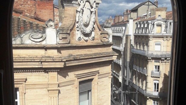 A view of a building with ornate architectural details, including a decorative crest and a balcony with wrought iron railings.